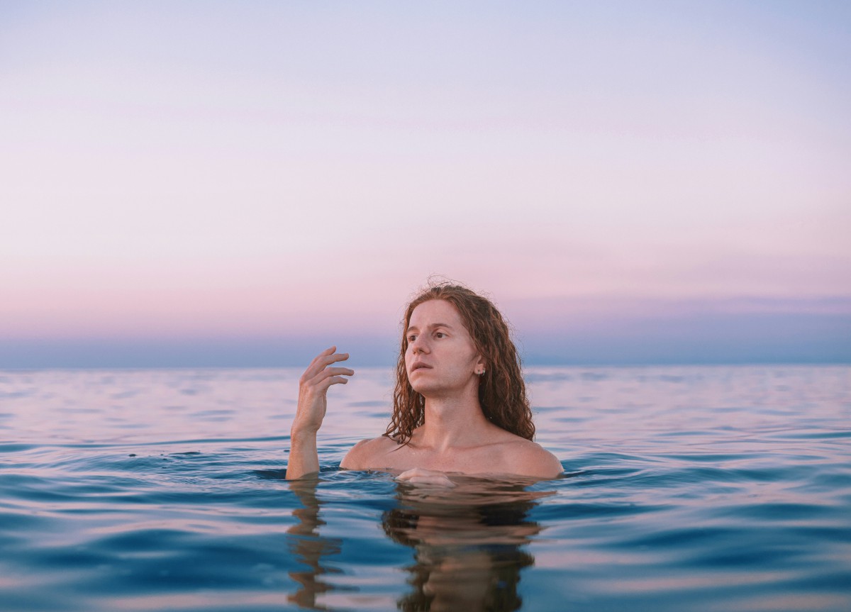 A woman floats in the ocean, reaching out with her hand, surrounded by tranquil blue waters.